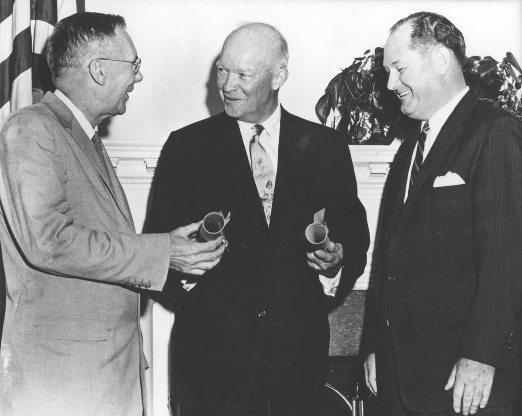 Three men standing together holding documents