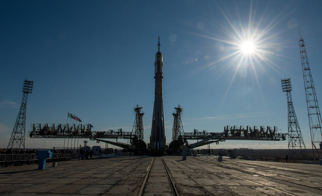 Soyuz spacecraft at launch pad with tower and bright sun in upper right
