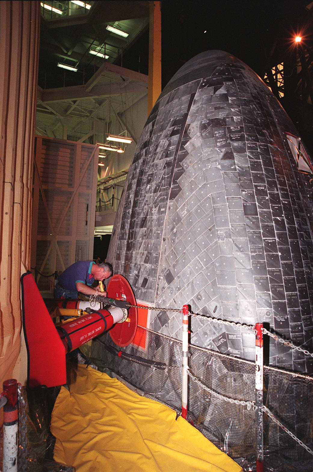 View of black tile covered bottom of shuttle Discovery with technician working at left