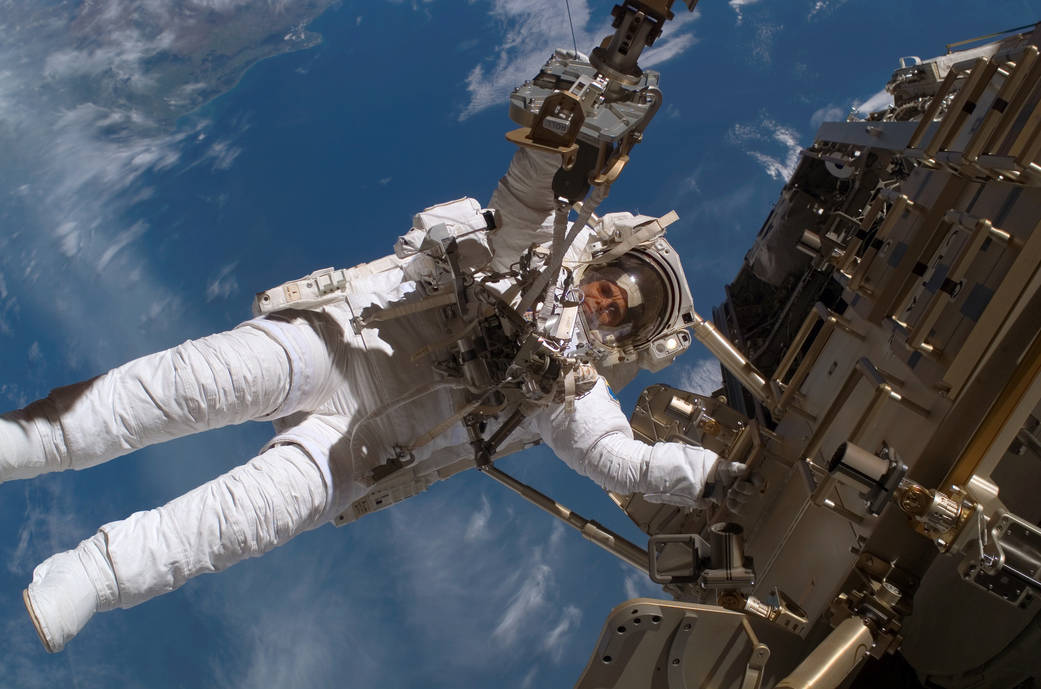 Closeup from below of spacewalking astronaut working on space station module with Earth in background