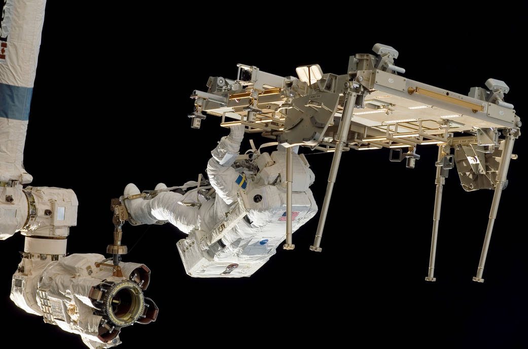 Astronaut on spacewalk upside down working on station module