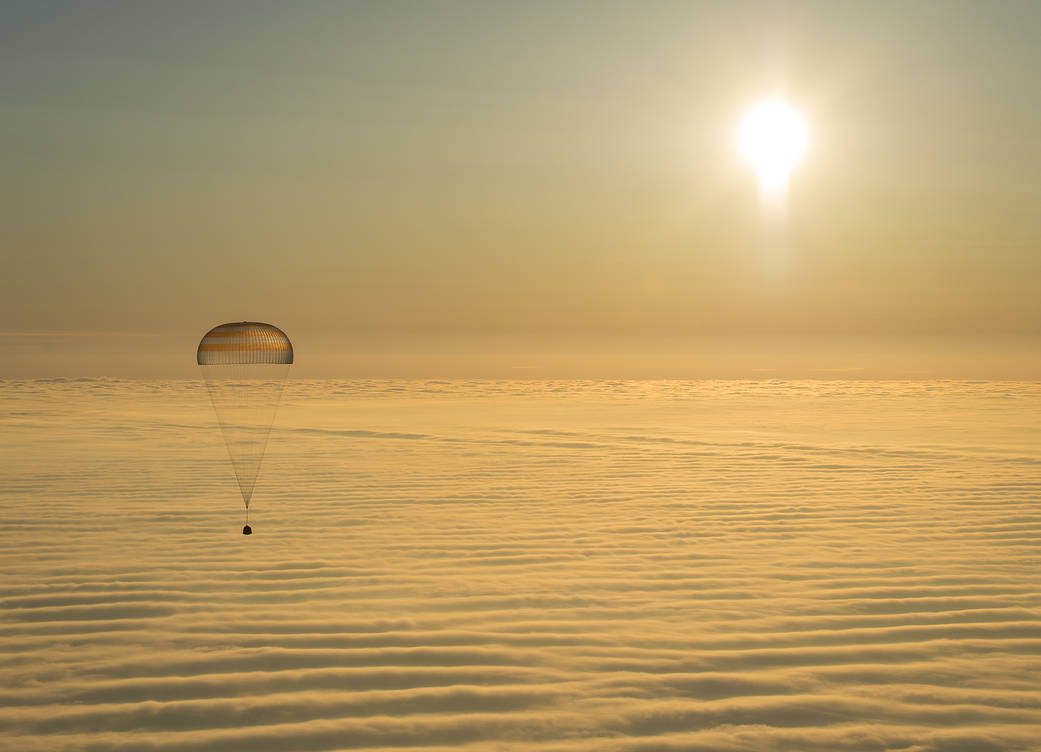 Soyuz capsule with parachute descends through clouds with sun above