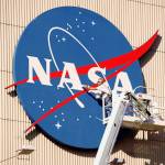 A person stands in a mechanical lift while painting a NASA meatball logo, which is at the top of the aircraft hangar. 
