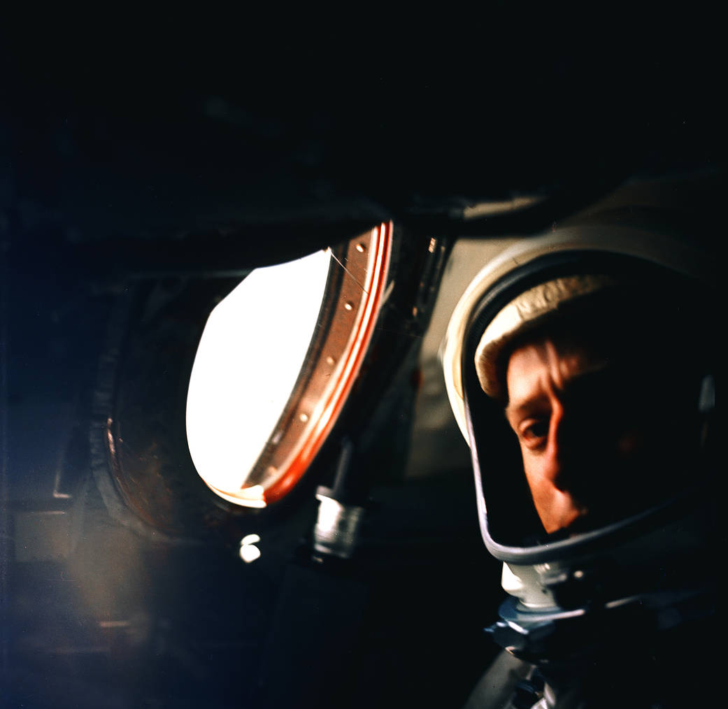 Astronaut inside Gemini V spacecraft next to portal window