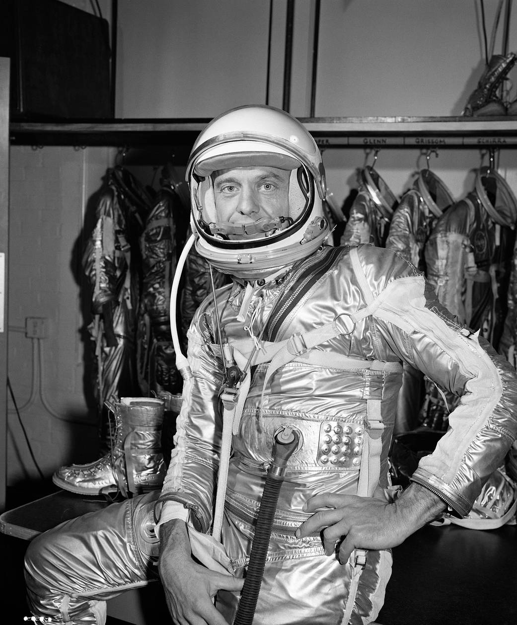 Closeup photo of astronaut Alan Shepard in pressure suit indoors with rack of pressure suits in background