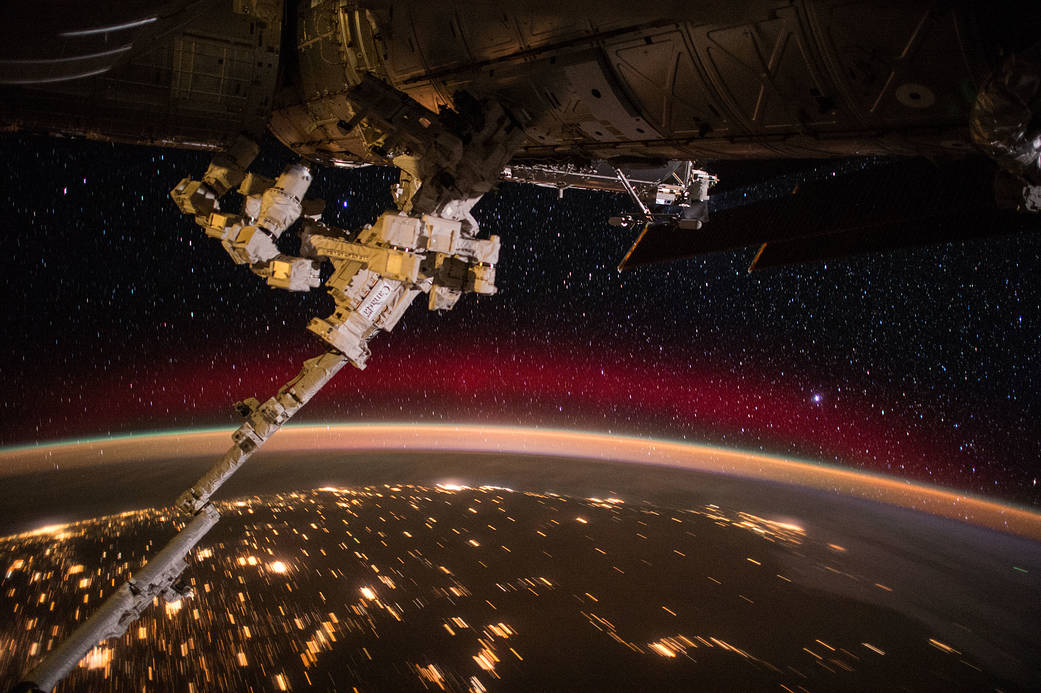 Space station robotic arm with curve of Earth and nighttime lights and aurora below