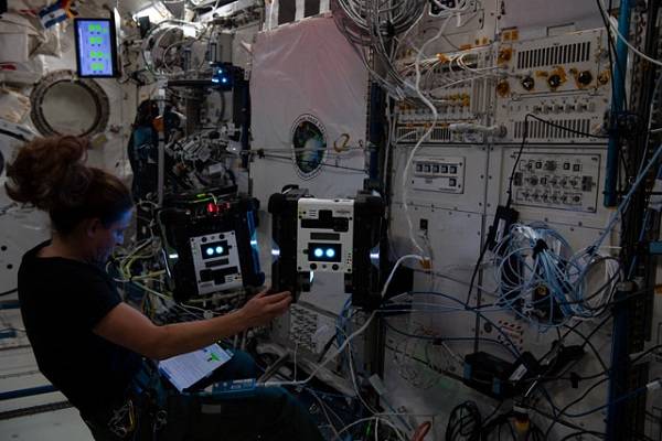 image of an astronaut working with flying robots inside the space station