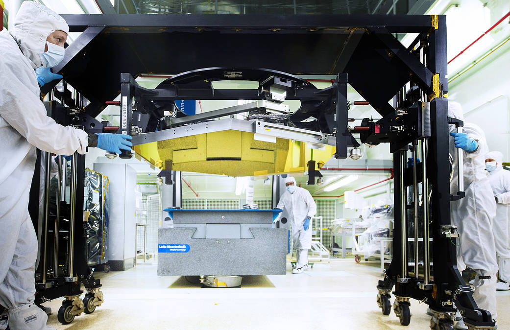 Gold hexagonal mirror segment on large frame with technicians in clean suits