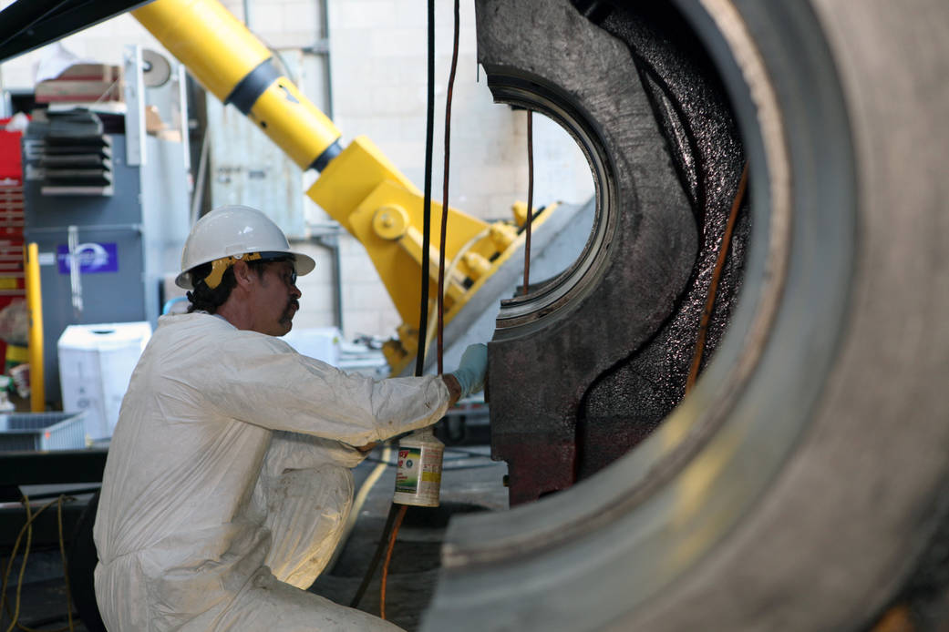 A ground support technician works on hardware in between the front treads of the crawler-transporter 2.