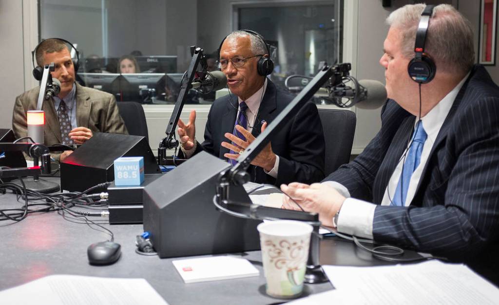 Administrator Bolden and two others seated at table speaking into radio microphones