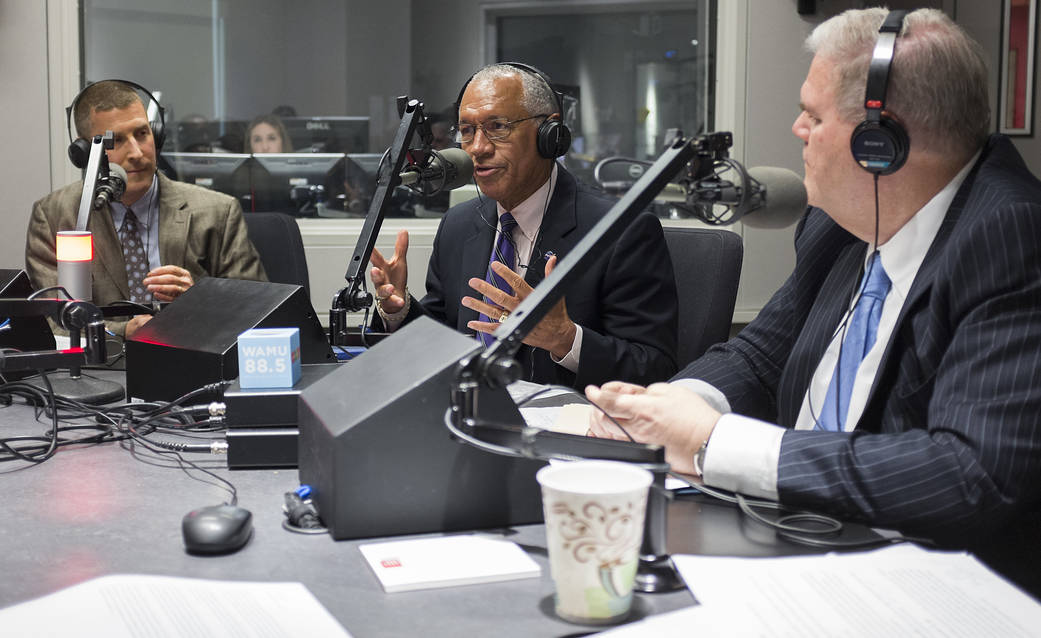 Administrator Bolden and two others seated at table speaking into radio microphones