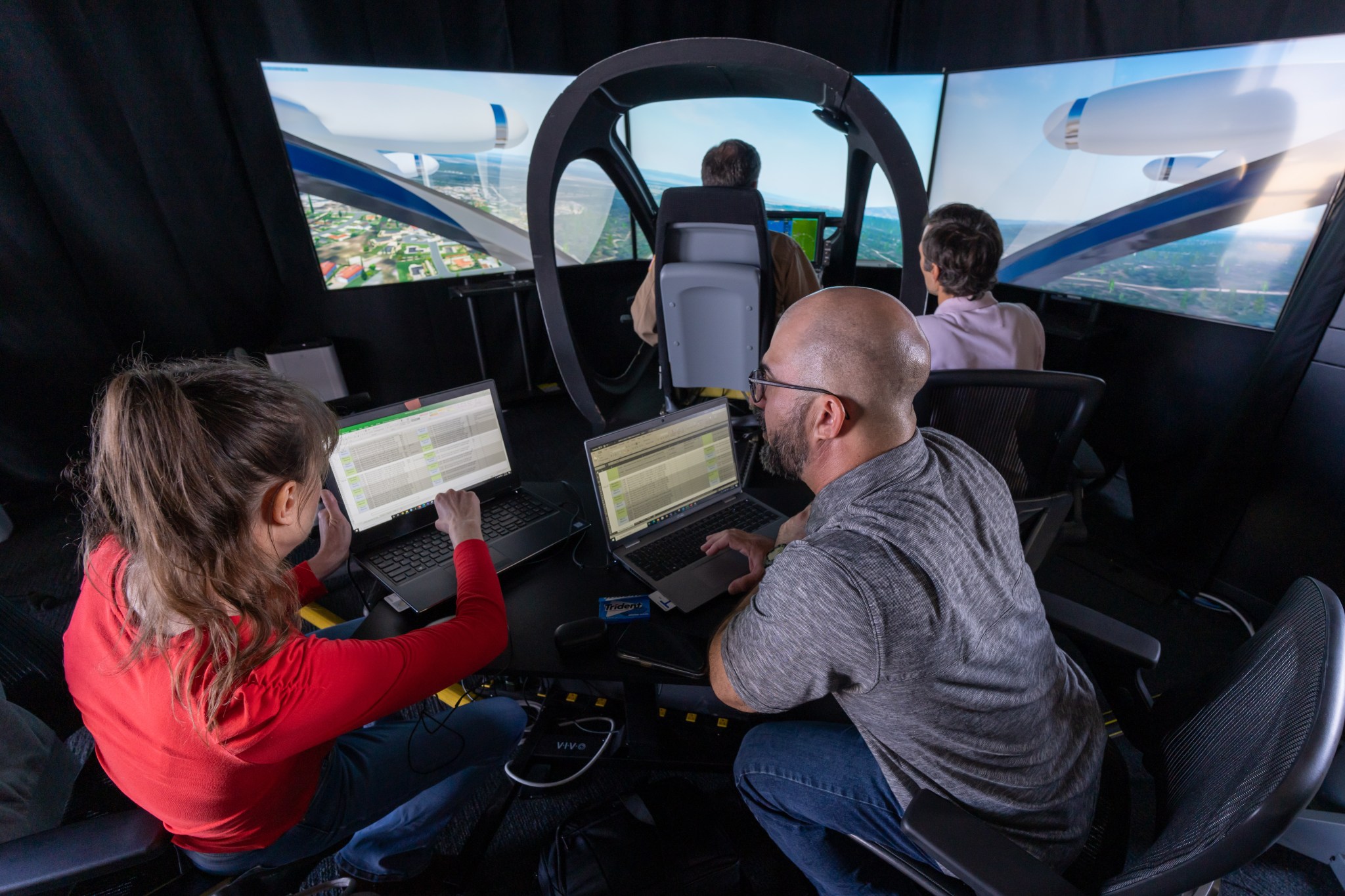 Federal Aviation Administration (FAA) data scientist Sarah Eggum, left, and FAA Unmanned Aircraft System Integration Office program manager Brad Drake analyze flight altitude data on Sept.19 in Marina, California. In the background, NASA research pilot Wayne Ringleberg and NASA project operations engineer Andrew Guion execute flight paths in Joby Aviation’s S4 simulator.