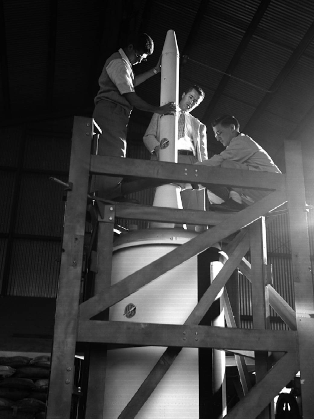 Three men standing at top of Explorer 1 satellite before launch