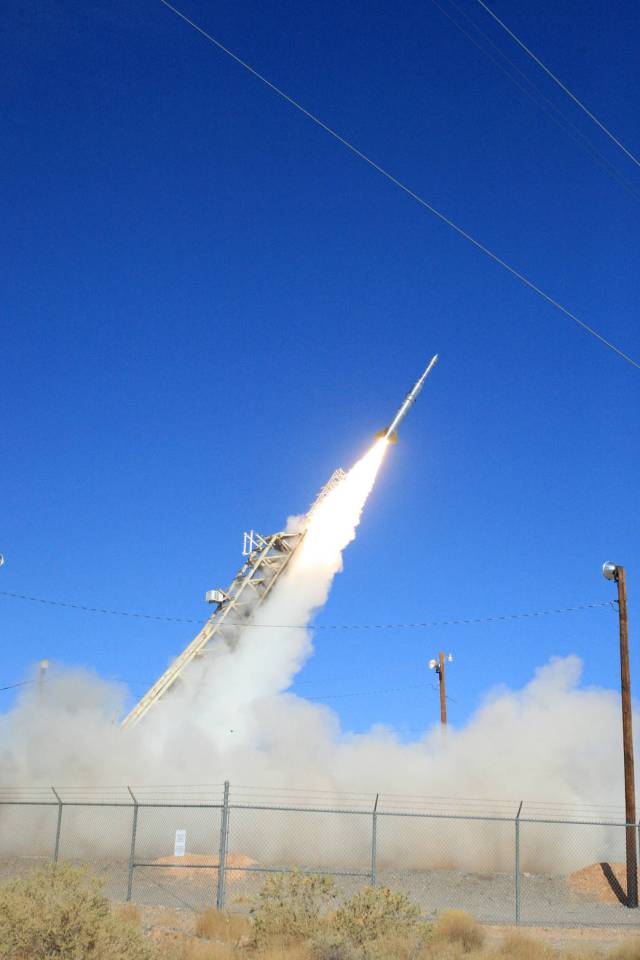 A small rocket launching with a plume of white smoke underneath against a blue sky.