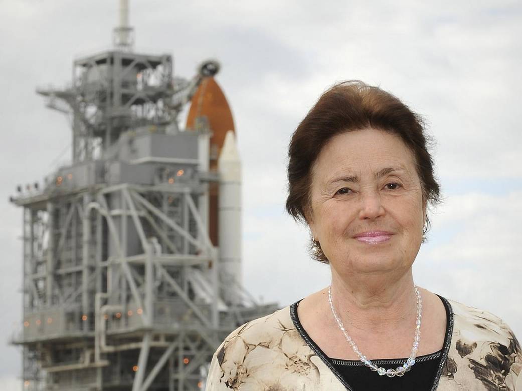 Woman poses for portrait with space shuttle at launch pad in the far background