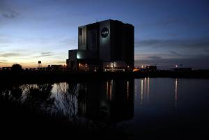 The dark water of the turn basin at NASA's Kennedy Space Center in Florida mirrors the night lights as the Vehicle Assembly Building and Launch Control Center are silhouetted against the post-sunset sky.
