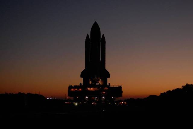 As the sun rises over Kennedy Space Center in Florida, a crawler transporter moves space shuttle Atlantis, secured atop a mobile launch platform, along the crawlerway from the Vehicle Assembly Building to Launch Pad 39A. 