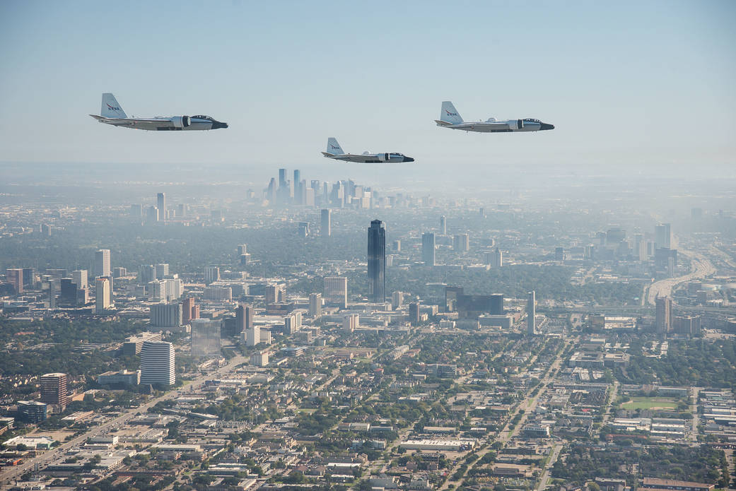 Three WB-57s flying over fog with skyscrapers of downtown Houston in background