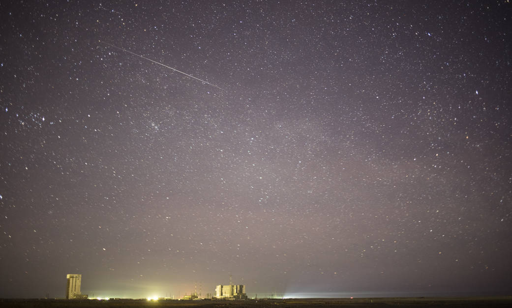Starry night sky with meteor streaking across, with launch pad visible at ground level