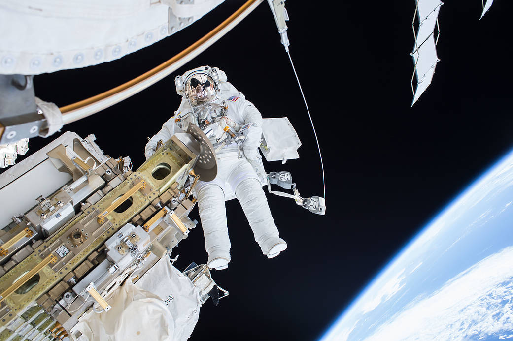 Astronaut in spacesuit floating outside International Space Station with Earth visible in lower right corner