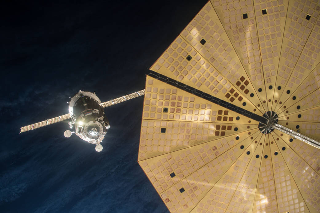 Soyuz spacecraft with solar arrays deployed at left approaching with round solar arrays of Cygnus in foreground right