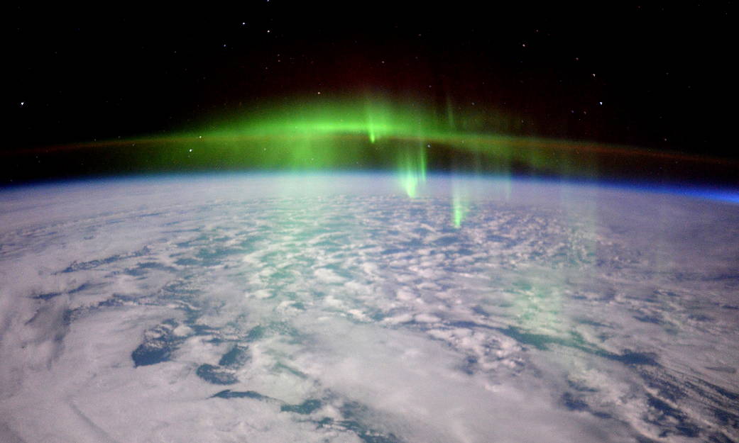 Glowing green aurora over clouds on Earth photographed from orbit