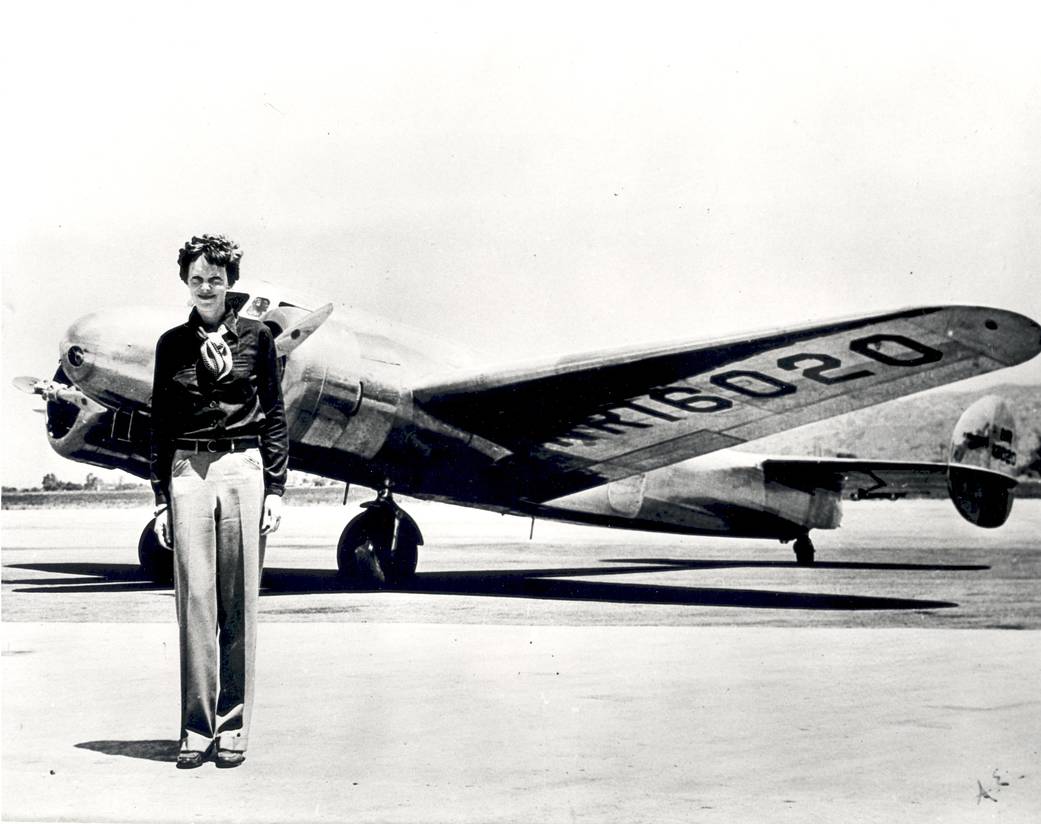 A black and white photo of Earhart standing in front of the Lockheed Electra aircraft.