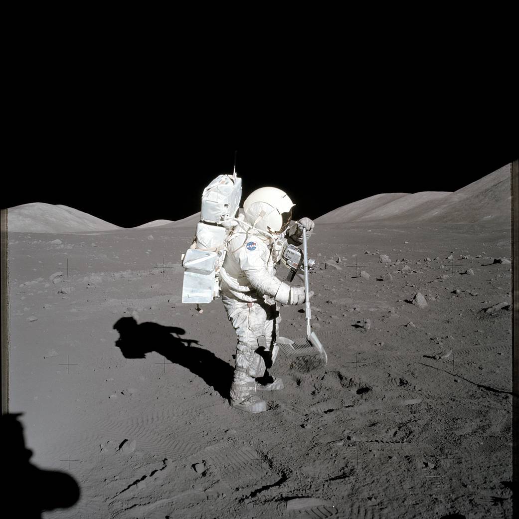Astronaut in spacesuit on lunar surface using rake to collect samples