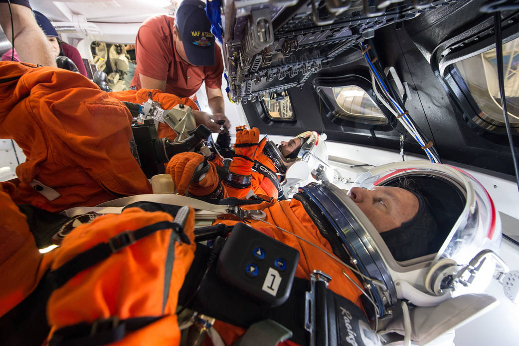 Crew in orange flight suits inside Orion spacecraft mockup