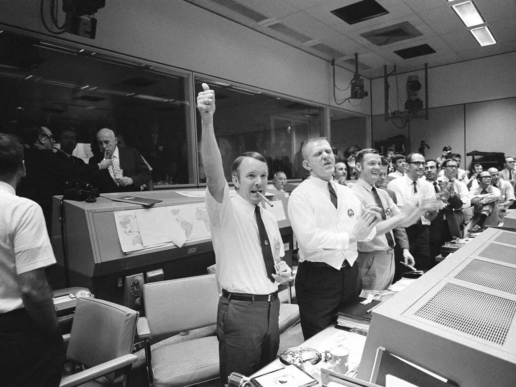 Flight directors in Mission Control cheering with arms in the air