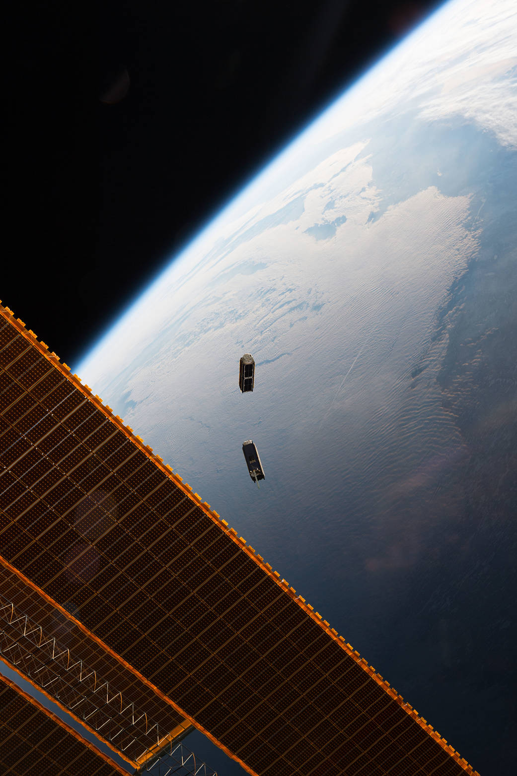Two Cubesats in space moments after release with space station solar array visible and Earth below