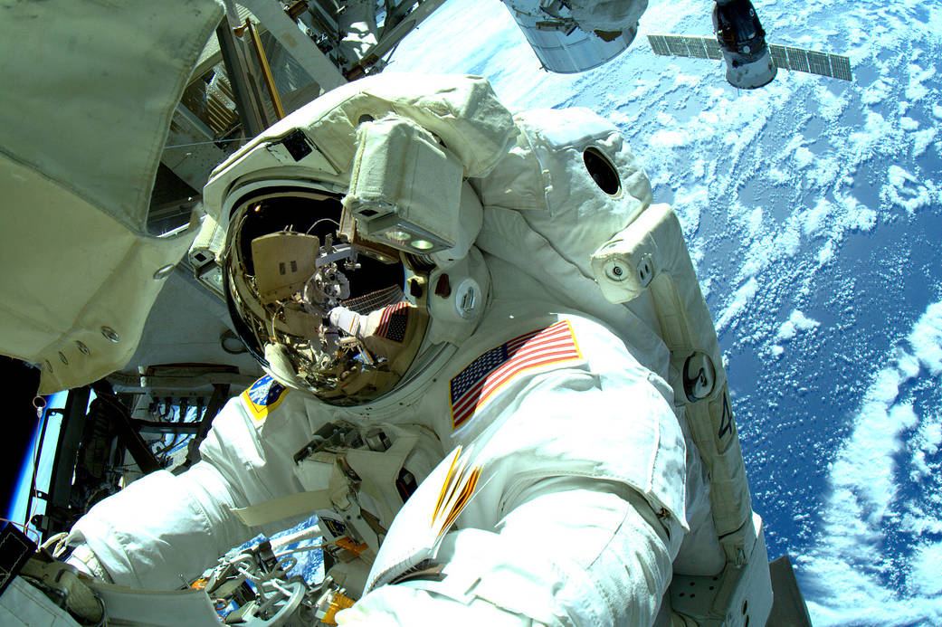 Terry Virts on a spacewalk with Earth visible in background and space station, fellow astronaut reflected in visor