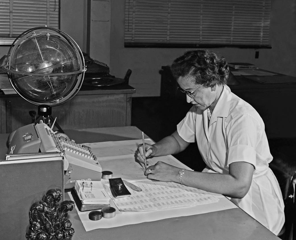 Katherine Johnson seated at desk working with globe at left