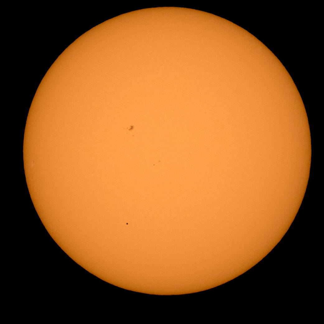 Full disc of the sun with tiny dot of planet Mercury visible as it travels across