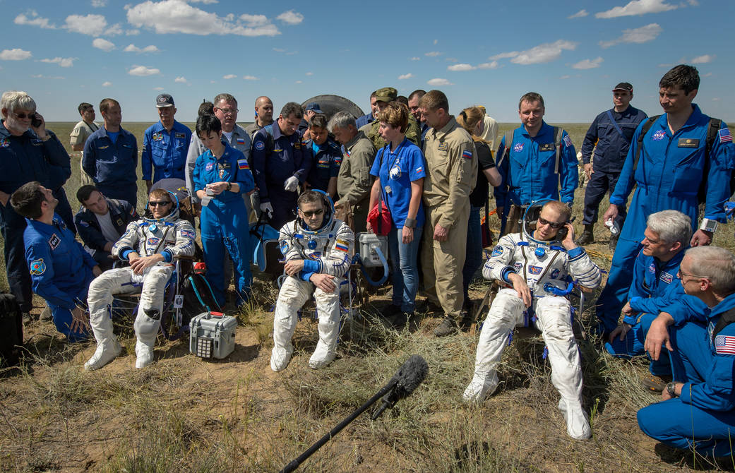 Three Expedition 47 crew members in Sokol suits seated, surrounded by officials, following landing