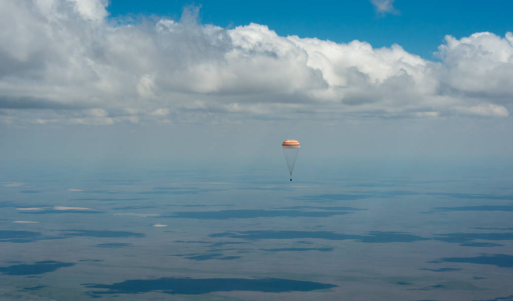 Soyuz capsule with parachute deployed descends through clouds