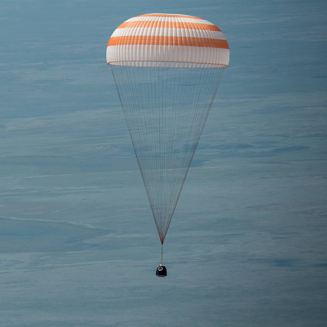 Soyuz capsule with parachute deployed descends toward Earth 