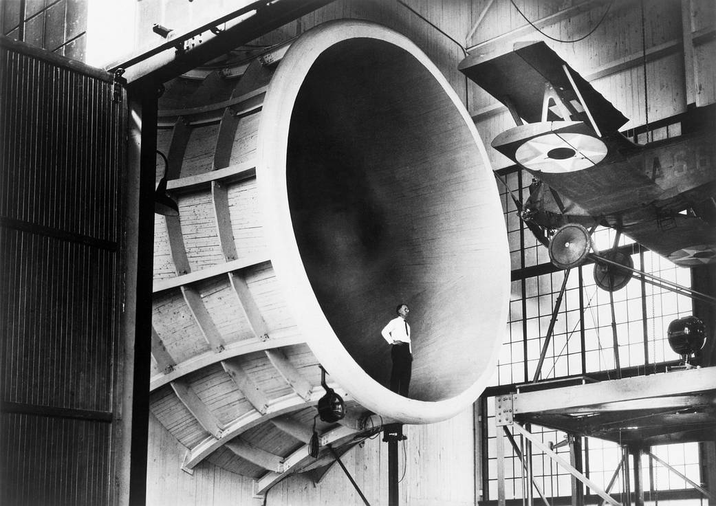 Man standing in giant wind tunnel with airplane suspended at upper right