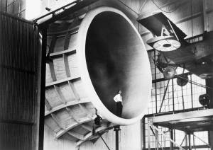 Man standing in giant wind tunnel with airplane suspended at upper right