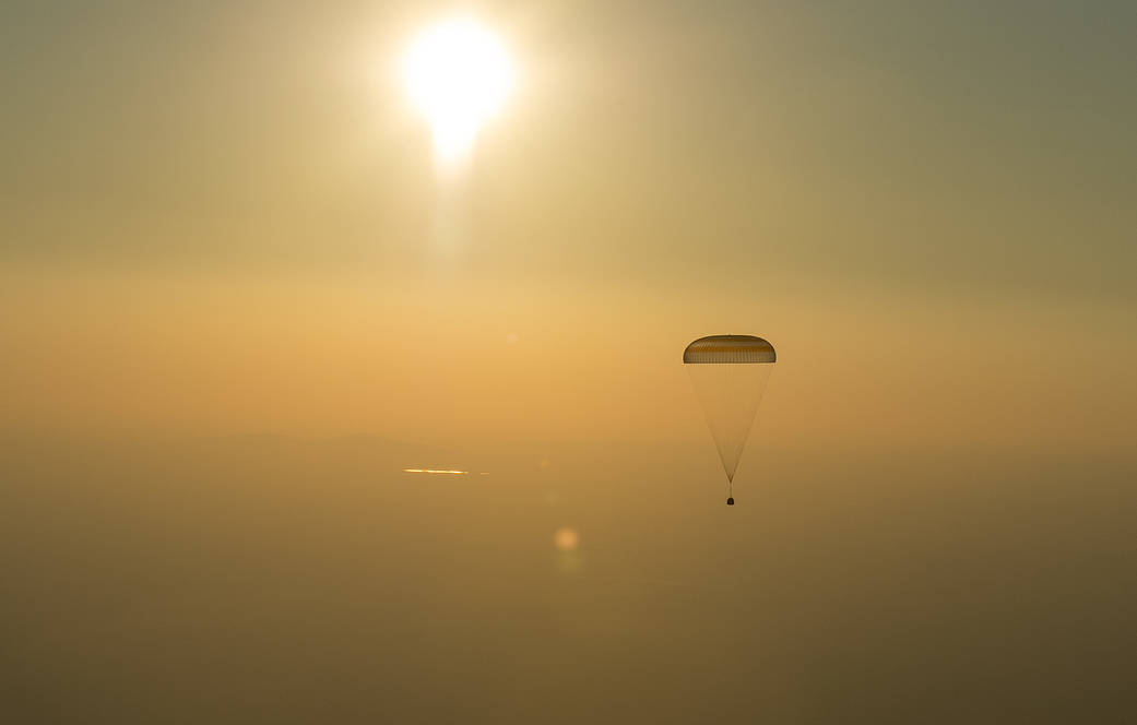 Soyuz capsule with parachute descends through clouds 