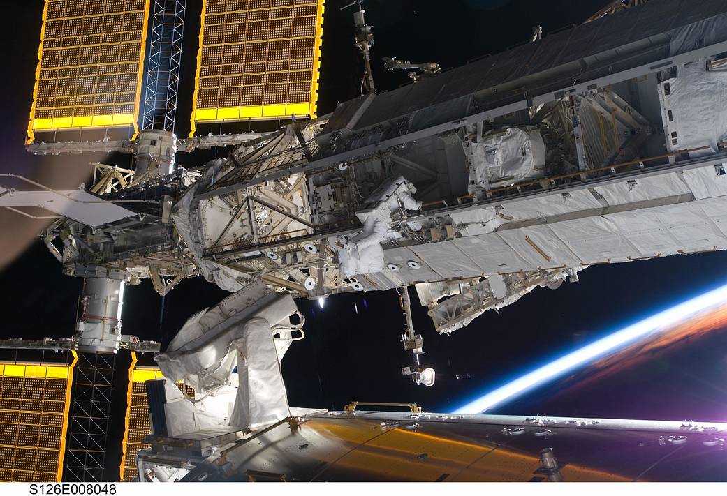Two spacewalking astronauts outside of space station laboratory module with truss and horizon in background