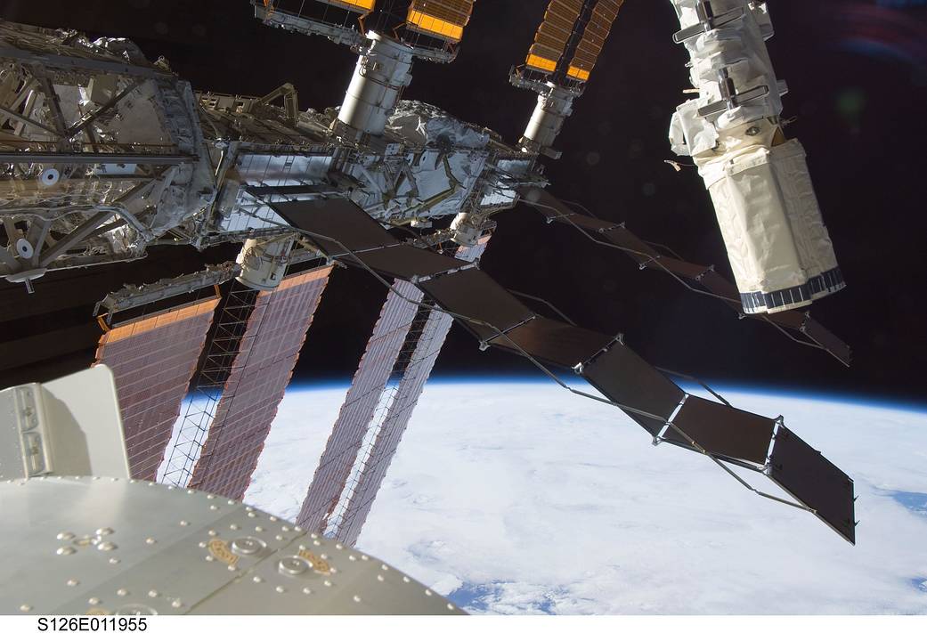 Side of shuttle Endeavour, robotic arm and solar arrays of International Space Station with Earth below