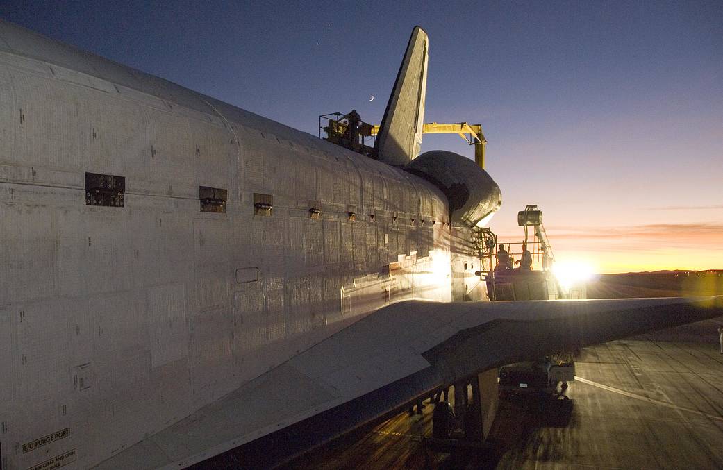 Bright floodlights resemble a sunset behind the wing of shuttle Endeavour on the runway