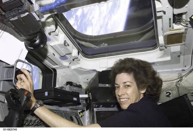 NASA astronaut Ellen Ochoa aboard space shuttle with window overhead looking out toward Earth