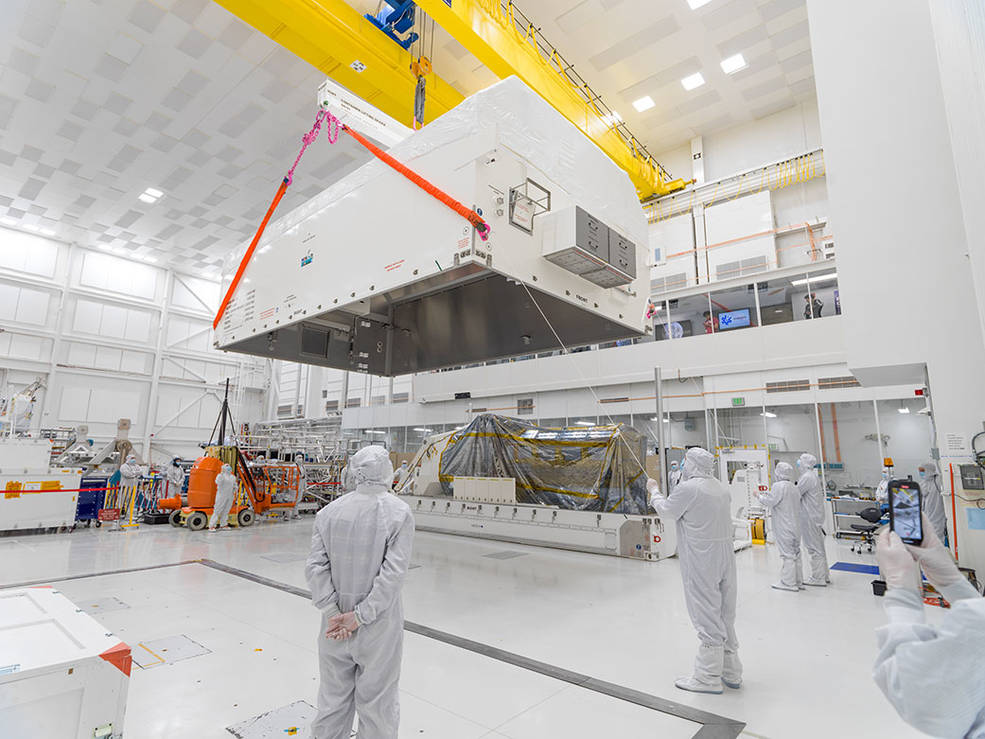 In a JPL clean room, engineers and technicians move the lid of container into position