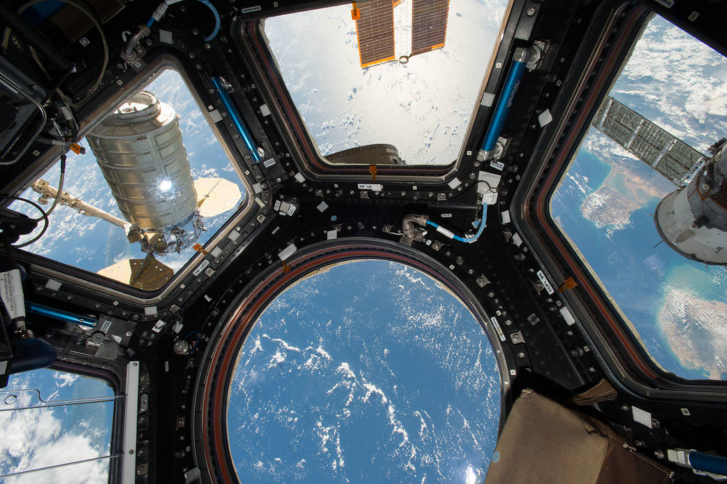 View from Cupola windows on space station with Cygnus cargo ship visible at left and Earth below