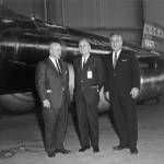 Three people in suits standing in front of the X-15 hypersonic aircraft.