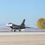 F-16XL aircraft landing, dragging a yellow parachute behind it.