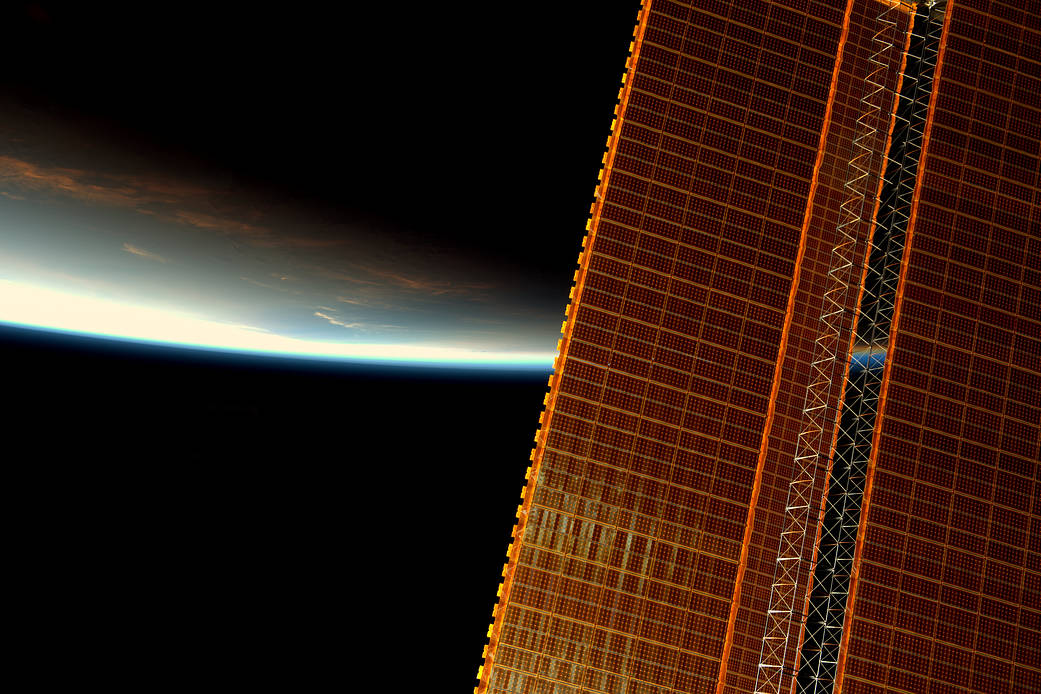 Sunrise over Earth's horizon with space station solar array