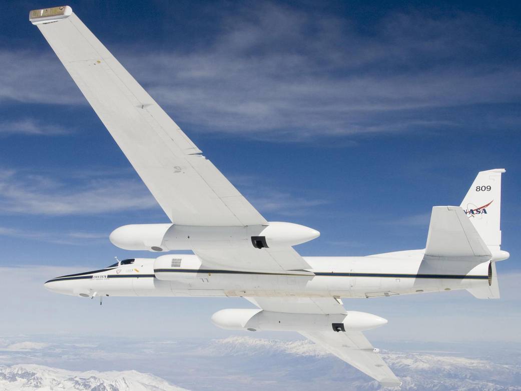 White NASA aircraft flies across blue sky among clouds